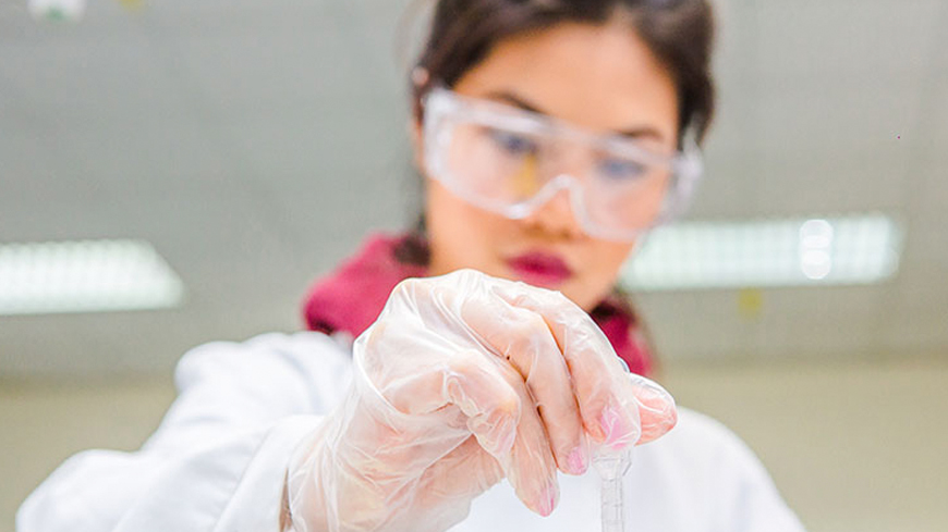 A person wearing PPE holds out a pipette