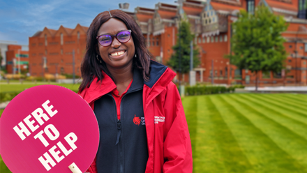 Student ambassador waiting to welcome guests with a sign that reads here to help.